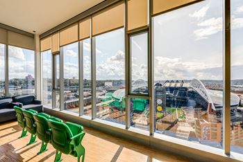 A room with green chairs and a view of a stadium through the windows.